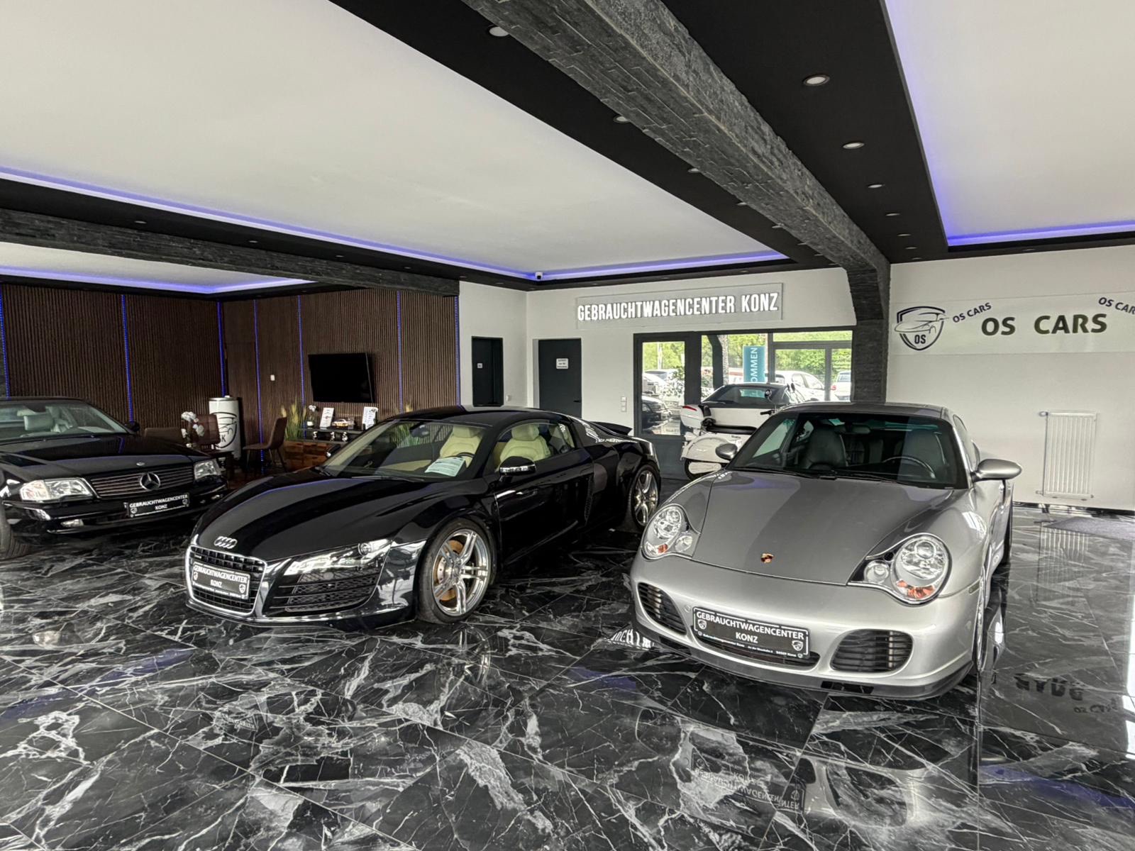 Gebrauchtwagencenter Konz — Showroom-Innenraum mit Audi R8, Porsche 911 und Mercedes-Benz auf Marmor-Boden